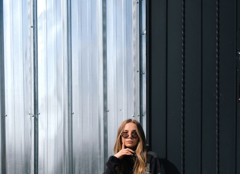 woman in black jacket and white pants sitting on gray concrete floor