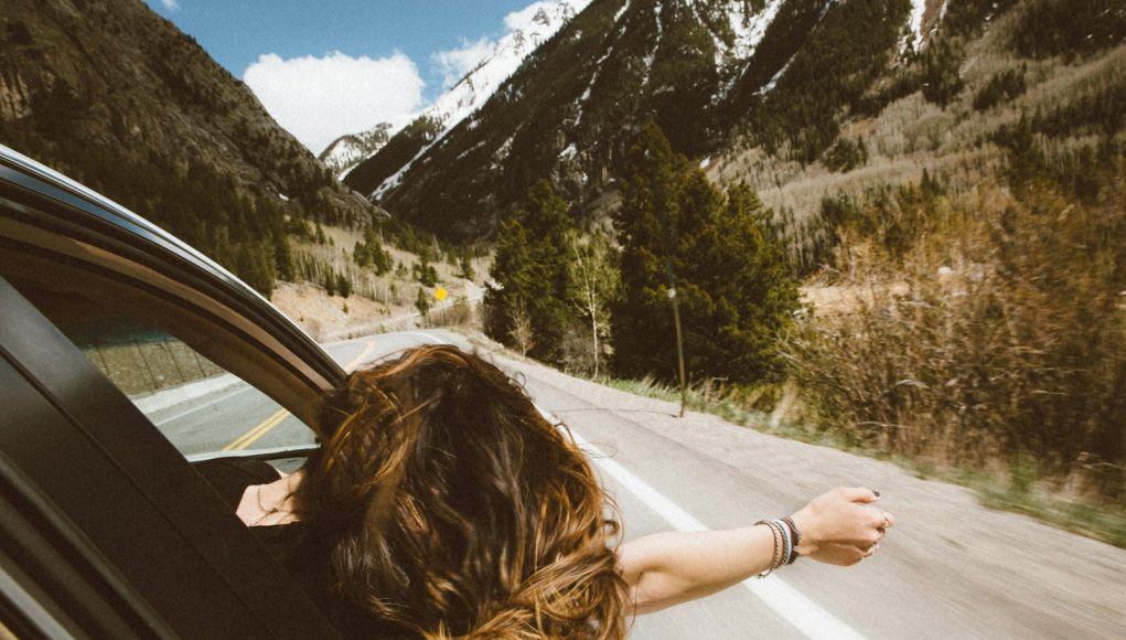 woman riding on vehicle putting her head and right arm outside the window while travelling the road