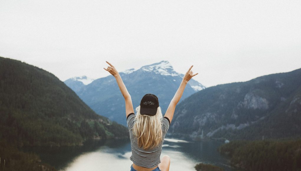woman sitting on cliff raising both hands