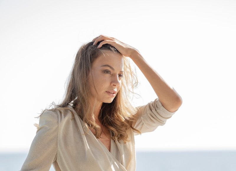woman in white long sleeve shirt and white pants sitting on white concrete wall during daytime