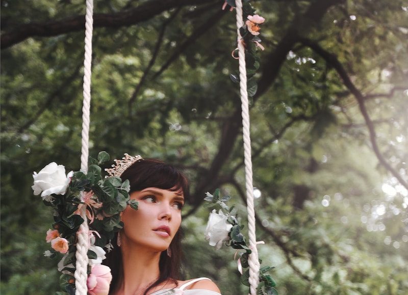woman wearing wedding gown sitting on outdoor swing near tall trees