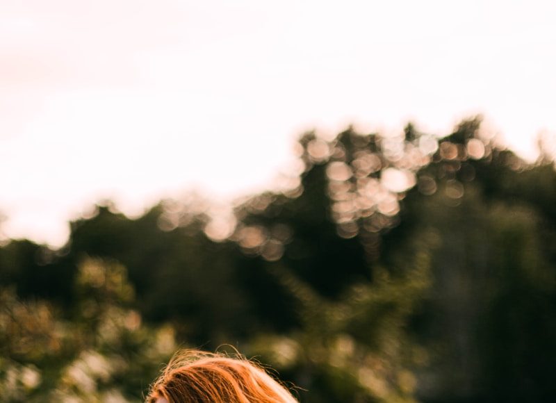 woman in white black and red floral sleeveless dress standing near green trees during daytime