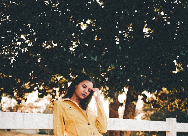 woman in white long sleeve shirt and black pants standing on white wooden fence during daytime